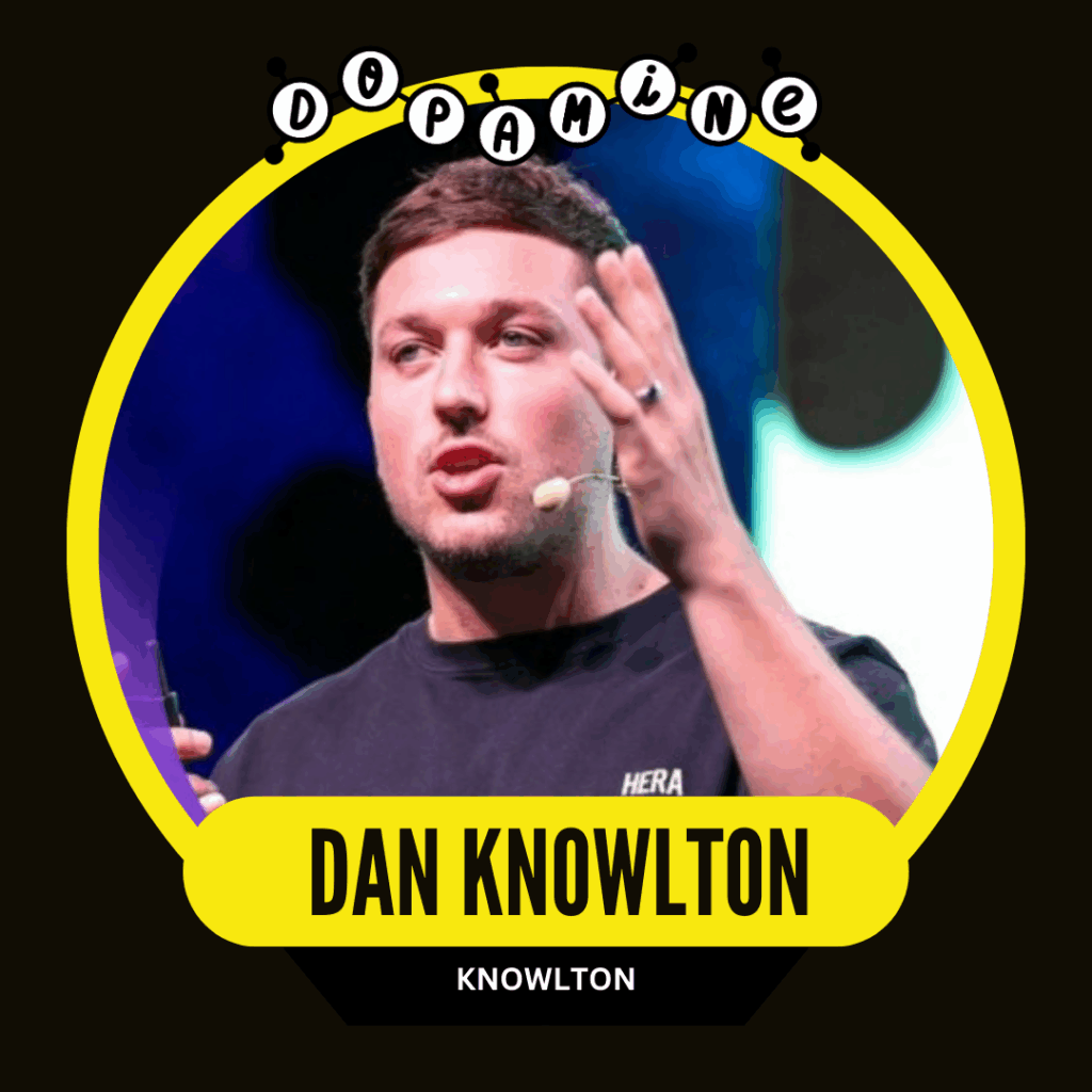 A man speaking animatedly on stage with a headset microphone and a colorful background, framed in a yellow and black circular graphic with the text "DOPAMINE" and "DAN KNOWLTON."