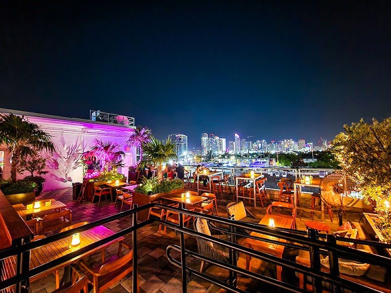 Rooftop bar with colorful lighting, ambient seating, and a view of a city skyline at night.