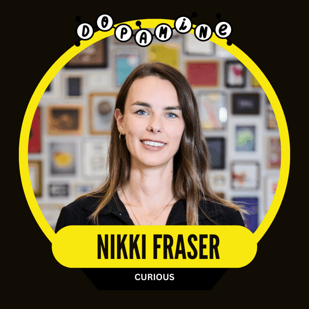 A woman with long brown hair smiles in front of a colorful, framed art wall. The image has a circular design labeled "Dopamine" at the top and a name plate "Nikki Fraser" with "Curious" below.