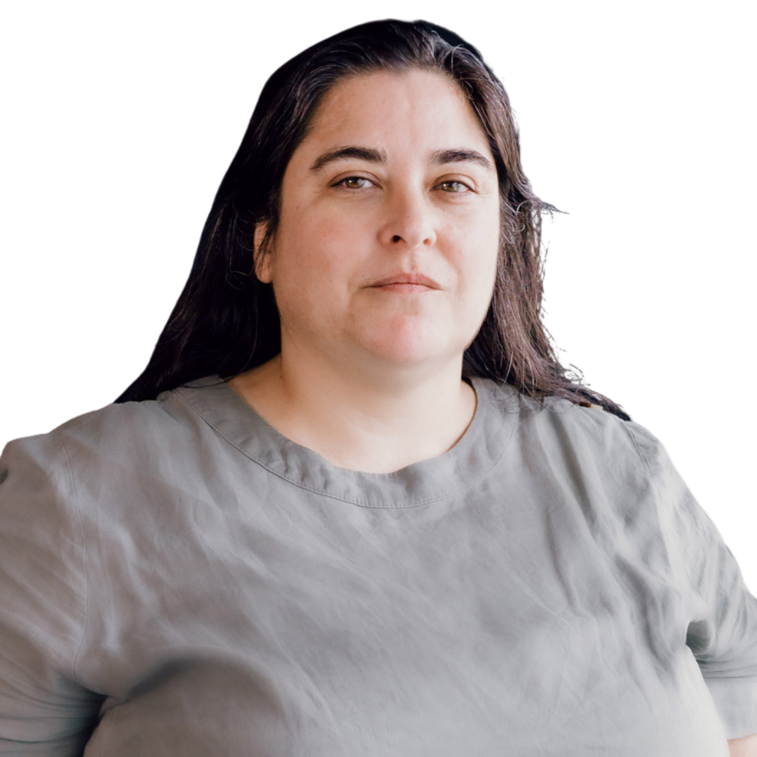 A woman with long dark hair stands confidently, wearing a simple gray shirt. She has a calm expression and is facing the camera, set against a light background.
