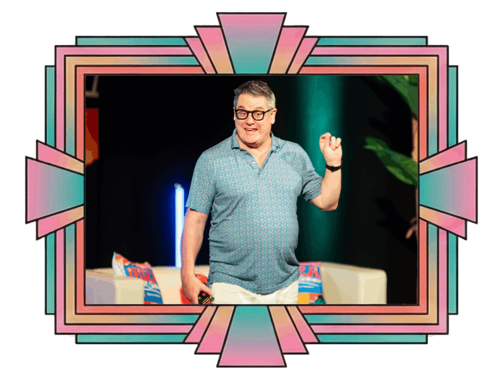 A smiling person in a casual shirt stands on stage with colorful, art deco-style borders surrounding the image.