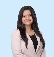 A woman with long dark hair smiles, wearing a light blazer over a black top, against a light blue background.