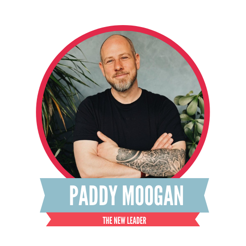 A man with crossed arms, wearing a black T-shirt, stands in front of a plant-filled background. The text reads "Paddy Moogan, The New Leader," set against a red backdrop with a circular frame.