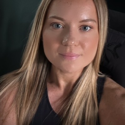 A woman with long blonde hair and a black top is looking at the camera with a slight smile.