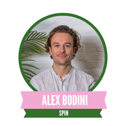 A person with short, brown hair, wearing a light-colored shirt, is in front of a white brick wall. The name "Alex Bodini" is displayed below, with "SPIN" included.