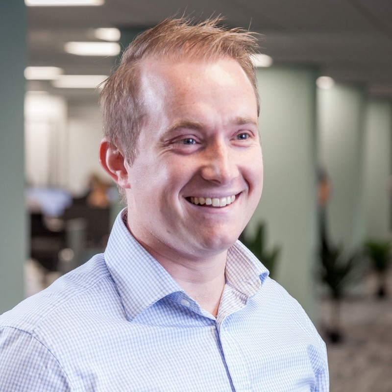 Smiling man in a white shirt standing in a modern office environment.