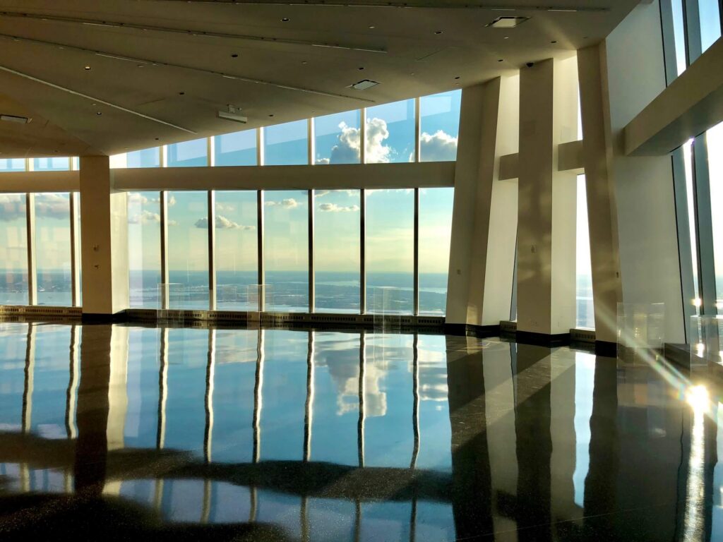 Spacious room with large windows overlooking a serene ocean view, with sunlight streaming in and reflecting on the shiny floor.