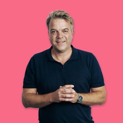 Smiling man in a navy polo shirt stands against a pink background.