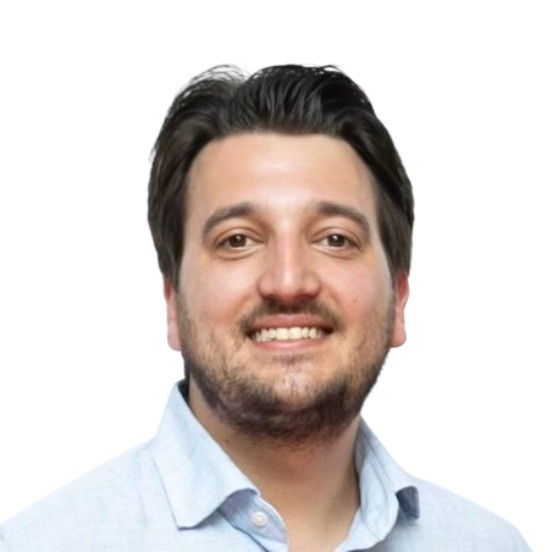 Smiling person with short brown hair and a beard, wearing a light blue collared shirt against a plain white background.