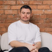 Man in a white shirt sitting on a couch against a brick wall.