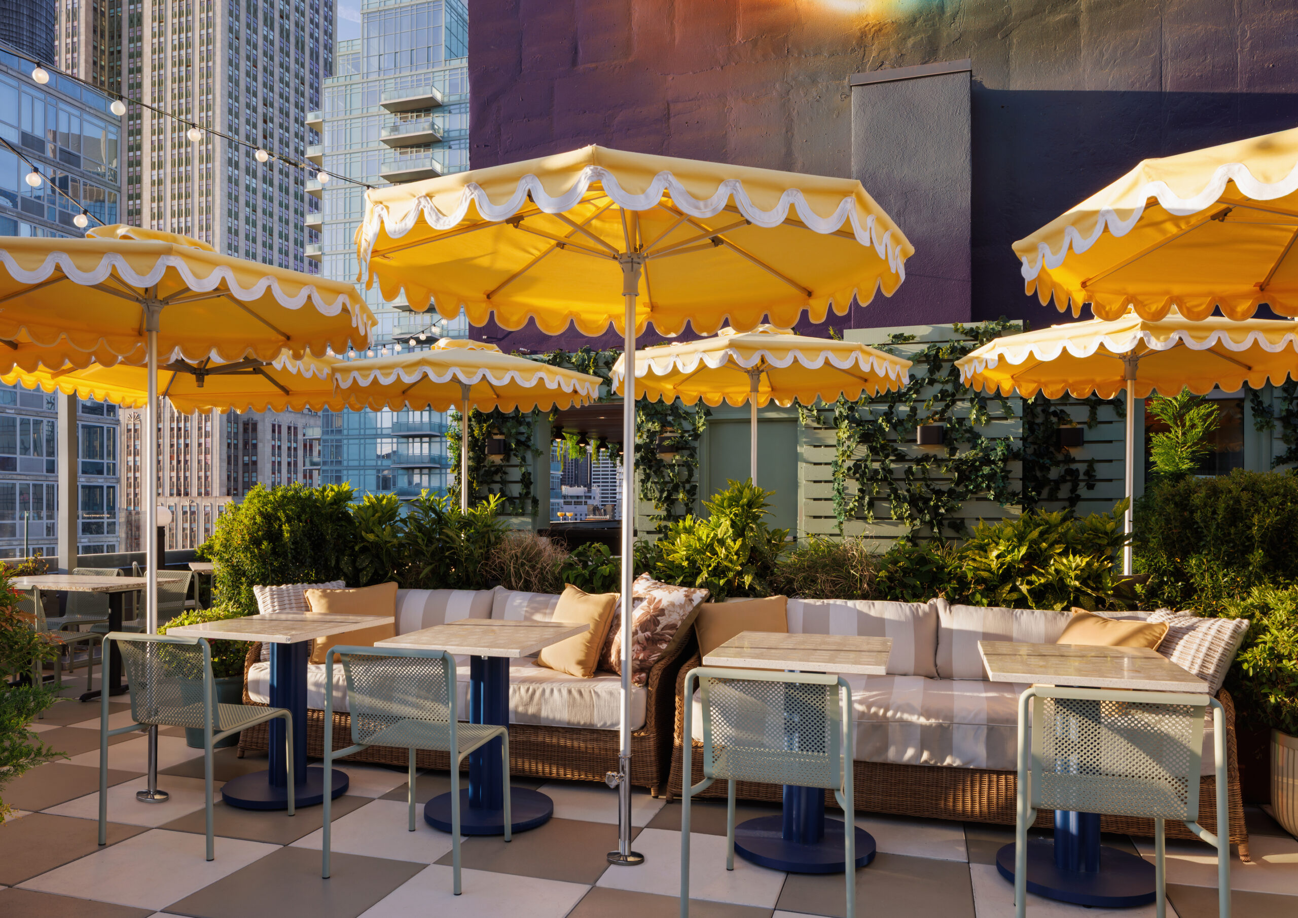 Rooftop patio with yellow striped umbrellas, cozy couches, glass tables, and city skyline in the background.
